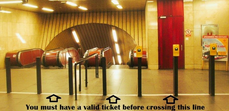 White line marking the entrance to Prague Metro’s paid area, with yellow ticket validators before the escalators.