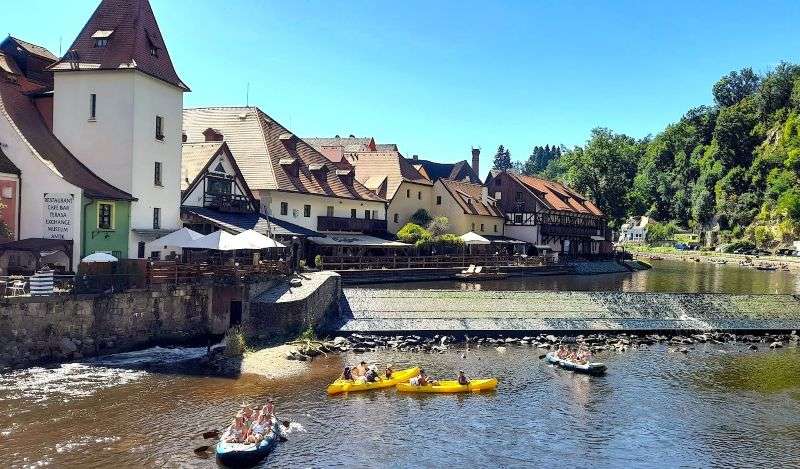 People paddling a yellow raft on the Vltava River with the historic old town buildings of Cesky Krumlov on the left