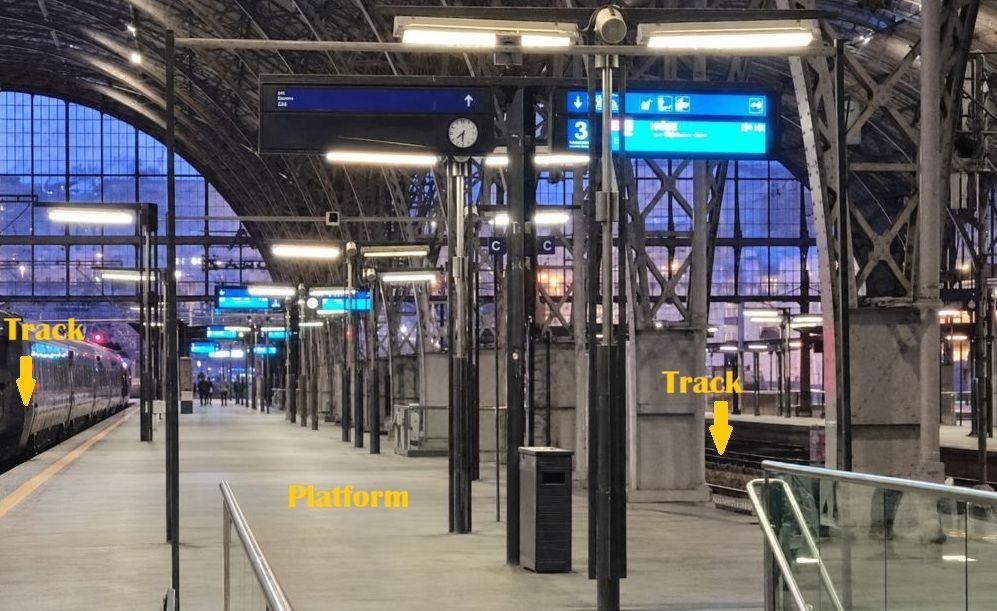Platform at Prague Main Train Station between two railway tracks, with a train standing on the left.