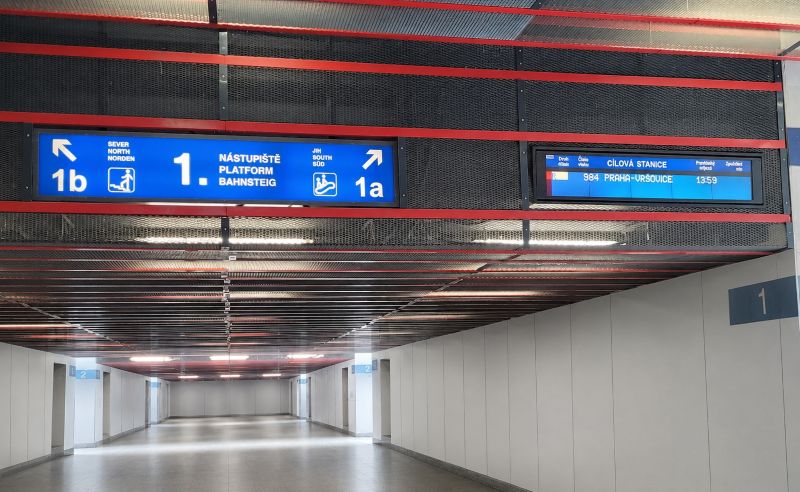 Overhead signs at Prague Main Station direct passengers to Platforms 1a and 1b, beside an electronic display showing the next departure from Platform 1.