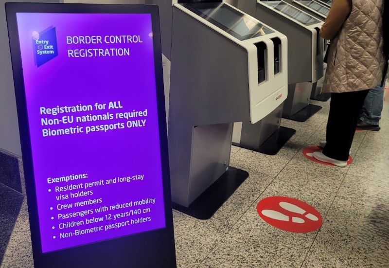 EES registration kiosks at Prague Airport arrivals, beside a sign listing registration requirements and exemptions.