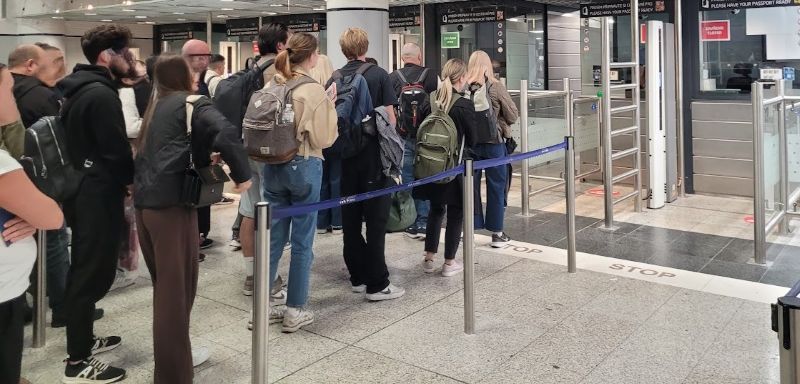 Passengers waiting in line at staffed passport-control counters in Prague Airport’s Terminal 1 arrivals area.