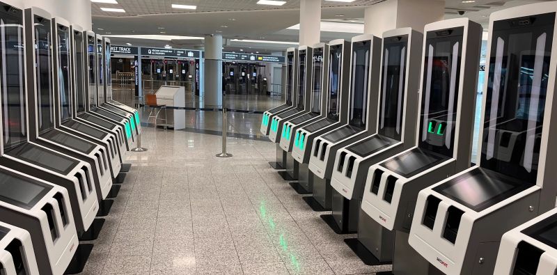 Rows of EES self-service kiosks with passport-control counters in the background at Prague Airport Terminal 1.